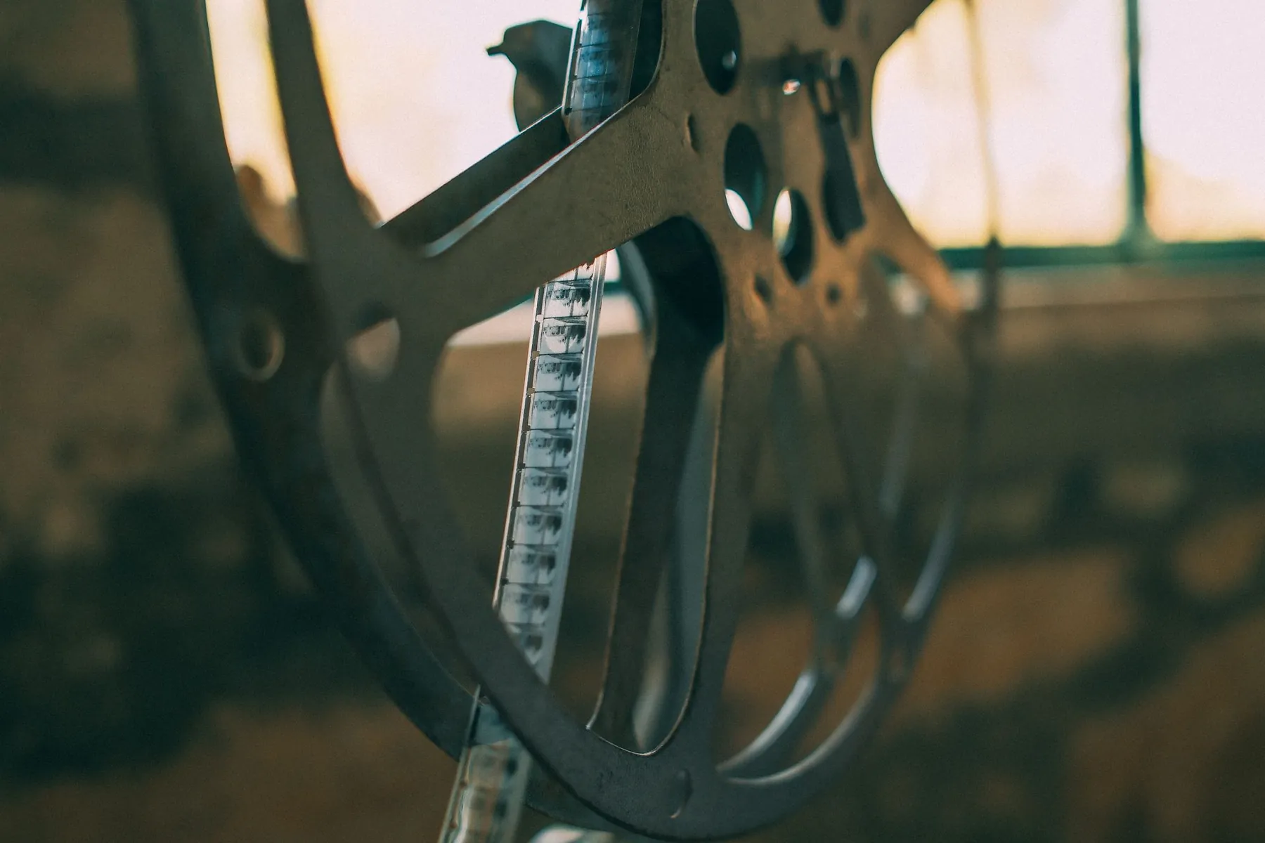 A metal film reel with a strip of home movie film hanging from it, lit by window light